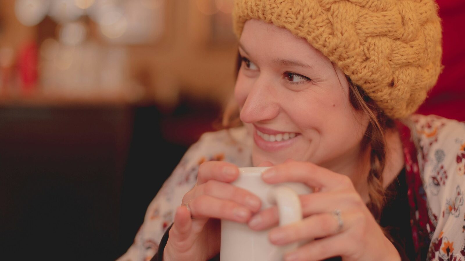 woman in brown knit cap holding white ceramic mug